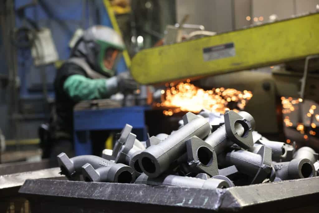 A photo of sand castings in a foundry. In the background, there's an employee grinding sand castings